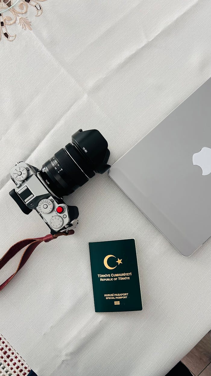 Flat lay of a camera, laptop, and Turkish passport on a white surface, ideal for travel themes.